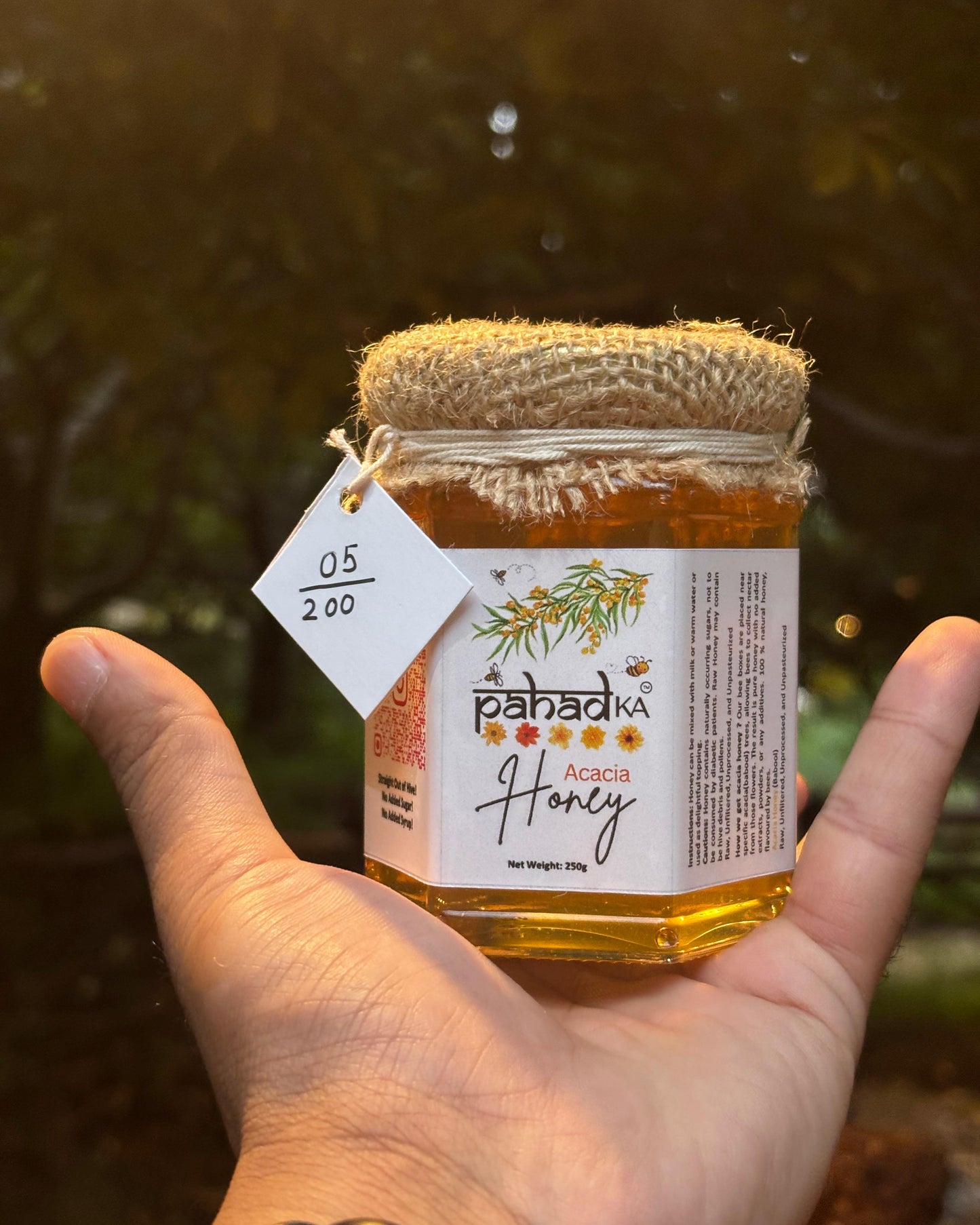 Hand holding a jar of Pahada Acacia Honey with a blurred natural background